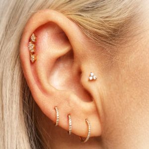 Mehrere Ohrpiercings mit goldfarbenem Schmuck und Steinen im professionellen Piercing Studio nahe Zwickau